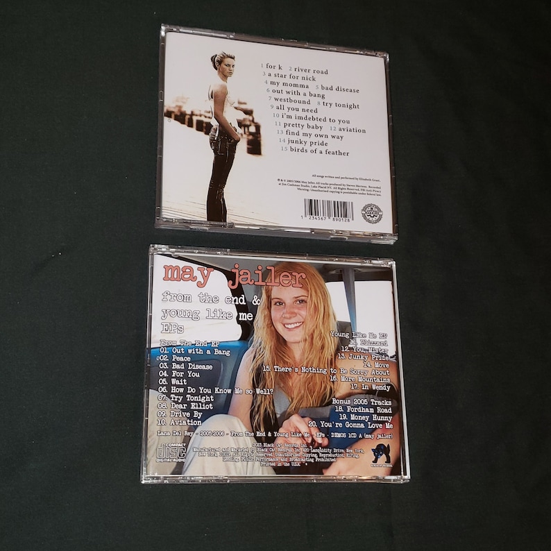 May include: A CD case with a black and white photo of a woman on the front. The title of the CD is "May Jailer" and the album is "From the End & Young Like Me". The back of the case lists the songs on the CD.