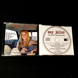 May include: A CD case with a photo of a young woman on the front cover. The CD case is for the album "From the End & Young Like Me EP" by May Jailer. The back of the case lists the songs on the album.