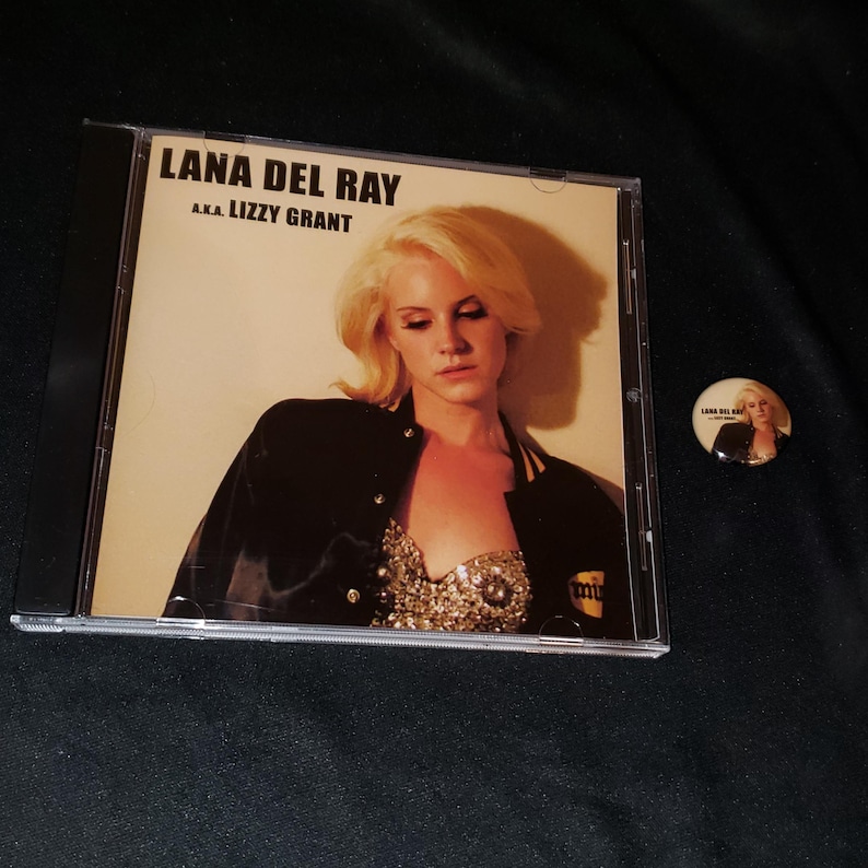May include: A CD case with a photo of Lana Del Rey on the cover. The text on the cover reads "Lana Del Rey AKA Lizzy Grant".