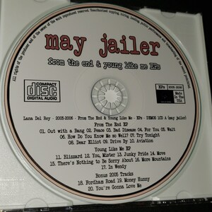 May include: A white CD with a black and red label. The label has the text "may jailer" in a large font, followed by "from the end & young like me EPs" in a smaller font. The CD also has a small sticker with the text "EPS 2005-2006" and "Made In The USA". The CD contains a collection of songs by Lana Del Rey.