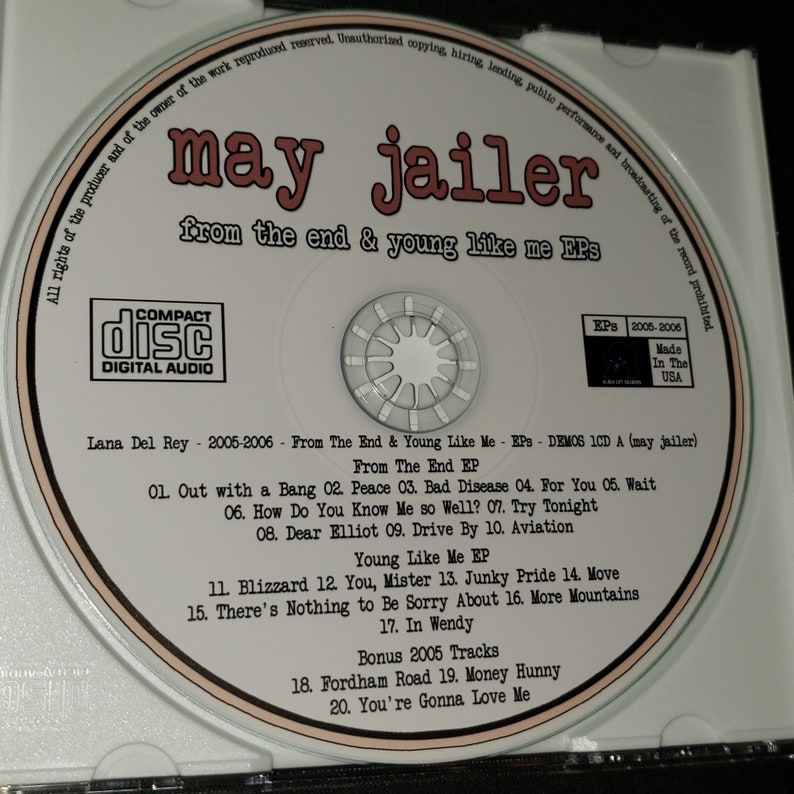 May include: A white CD with a black and red label. The label has the text "may jailer" in a large font, followed by "from the end & young like me EPs" in a smaller font. The CD also has a small sticker with the text "EPS 2005-2006" and "Made In The USA". The CD contains a collection of songs by Lana Del Rey.