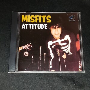 May include: A CD case with a black background and a yellow and white Misfits logo. The text "Misfits Attitude" is printed in white. The image shows a person wearing a black and white skeleton costume singing into a microphone.