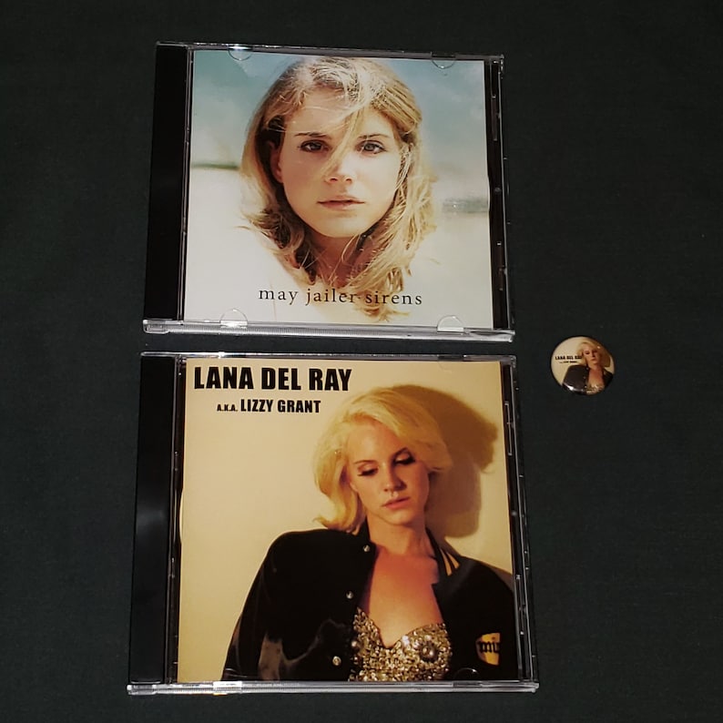 Puede incluir: Dos discos compactos con cajas negras. El CD superior presenta a una mujer con el pelo largo y rubio y el texto "may jailer sirens". El CD inferior presenta a una mujer con el pelo rubio y el texto "Lana Del Ray aka Lizzy Grant".