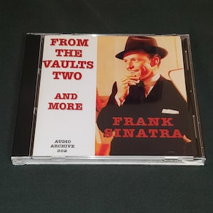 May include: A CD case with a red and white design. The front of the case features a photo of Frank Sinatra in a black suit and a fedora. The text "From The Vaults Two And More" is printed in red on the left side of the case. The text "Frank Sinatra" is printed in red on the right side of the case.
