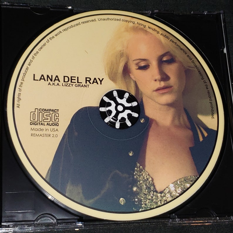 Puede incluir: Un CD con un retrato de Lana Del Ray, con el texto "LANA DEL RAY A.K.A. LIZZY GRANT" y "COMPACT DISC DIGITAL AUDIO Made in USA REMASTER 2.0".