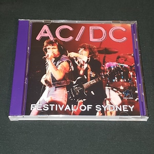 May include: A CD case with a pink and white AC/DC logo and the text "Festival of Sydney". The image shows a live performance of the band with two band members on stage.