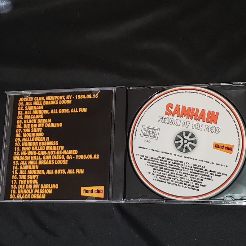 May include: A black CD case with a black and white image of a skull on the front. The case is labeled "Samhain Season of the Dead" and features the band's name in white text. The back of the case lists the tracklist for the album, which includes songs like "All Hell Breaks Loose", "Die Die My Darling", and "Unholy Passion".