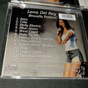 K&ouml;nnte beinhalten: Ein CD-Geh&auml;use mit einem Foto von Lana Del Rey, die beim Bravalla Festival in Schweden auftritt. Auf der R&uuml;ckseite des Geh&auml;uses sind die Songs auf der CD aufgelistet: Intro, Cola, Body Electric, Blue Jeans, West Coast, Born To Die, Young And Beautiful, Ultraviolence, Summertime Madness, Ride, Video Games und National Anthem.