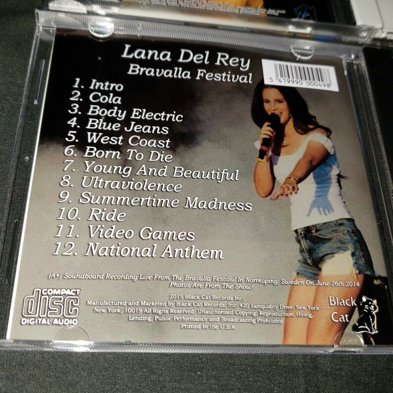 K&ouml;nnte beinhalten: Ein CD-Geh&auml;use mit einem Foto von Lana Del Rey, die beim Bravalla Festival in Schweden auftritt. Auf der R&uuml;ckseite des Geh&auml;uses sind die Songs auf der CD aufgelistet: Intro, Cola, Body Electric, Blue Jeans, West Coast, Born To Die, Young And Beautiful, Ultraviolence, Summertime Madness, Ride, Video Games und National Anthem.