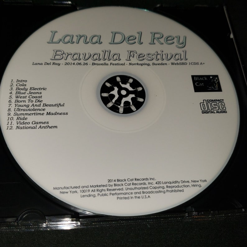 K&ouml;nnte beinhalten: Eine wei&szlig;e CD mit einem schwarz-wei&szlig;en Bild eines Sternenausbruchs in der Mitte. Der Text "Lana Del Rey Bravalla Festival" ist in Schwarz oben auf der CD gedruckt. Der Text "Lana Del Ray - 2014.06.26 - Bravalla Festival - Norrkoping, Schweden - WebSBD ICDS A+" ist in Schwarz unter dem Sternenausbruch gedruckt. Der Text "Black Cat" ist in Schwarz in einem kleinen Rechteck in der oberen rechten Ecke der CD gedruckt. Der Text "COMPACT DISC DIGITAL AUDIO" ist in Schwarz in einem kleinen Rechteck in der unteren rechten Ecke der CD gedruckt. Der Text "2014 Black Cat Records Inc." ist in Schwarz unten auf der CD gedruckt. Der Text "Manufactured and Marketed by Black Cat Records, Inc. 420 Lanquidity Drive, New York New York, 10019 All Rights Reserved. Unauthorized Copying, Reproduction, Hiring, Lending, Public Performance and Broadcasting Prohibited Printed in the U.S.A" ist in Schwarz unten auf der CD gedruckt.