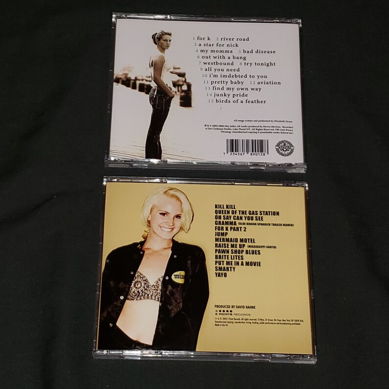 Puede incluir: Dos estuches de CD con fondo amarillo. La parte delantera del estuche presenta a una mujer con cabello rubio que lleva una blusa negra y un sujetador blanco. La parte posterior del estuche enumera los t&iacute;tulos de las canciones "Kill Kill", "Queen of the Gas Station", "On Say Can You See", "Gramma", "For K Part 2", "Jump", "Mermaid Motel", "Raise Me Up", "Pawn Shop Blues", "Brite Lites", "Put Me in a Movie", "Smarty" y "Yayo".