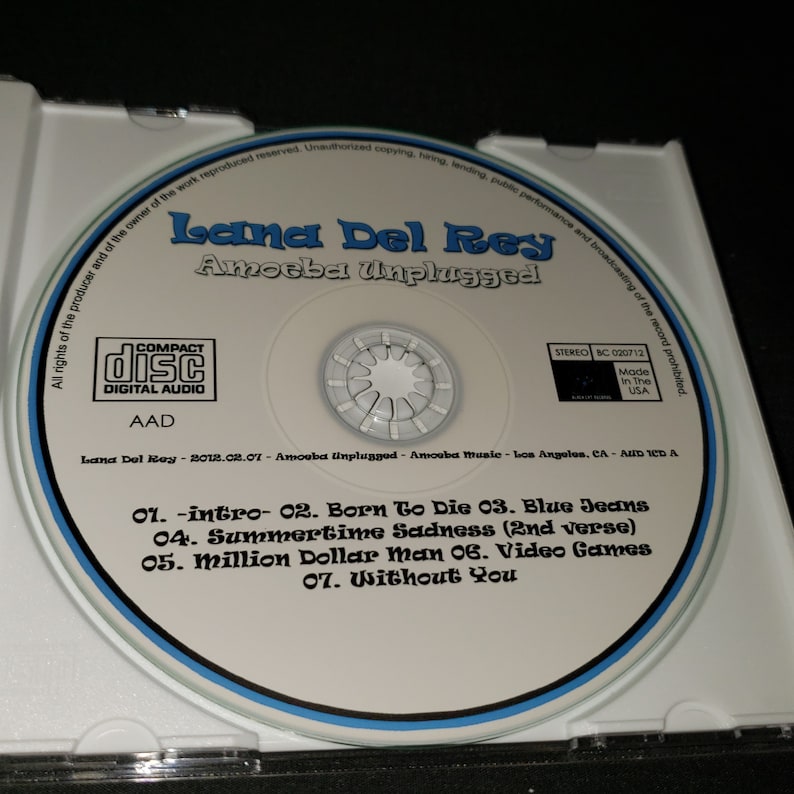 K&ouml;nnte beinhalten: Eine Compact Disc mit einem blauen und wei&szlig;en Rand. Die Disc hat ein wei&szlig;es Label mit dem Text "Lana Del Rey Amoeba Unplugged" in Schwarz. Die Trackliste ist unter dem Titel gedruckt: "01. -intro- 02. Born To Die 03. Blue Jeans 04. Summertime Sadness (2nd verse) 05. Million Dollar Man 06. Video Games 07. Without You".