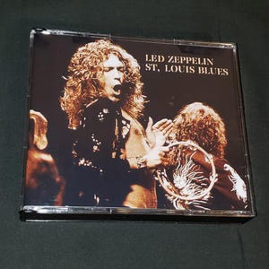 May include: A CD case with a black and white photo of a rock band. The text on the case reads "LED ZEPPELIN ST. LOUIS BLUES".