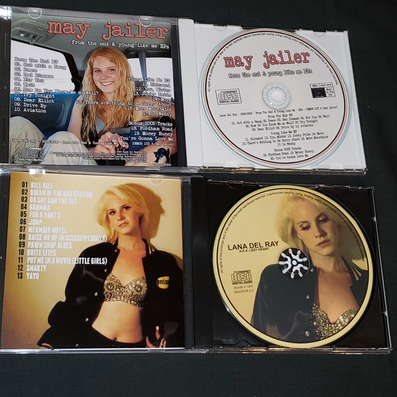 May include: Four CD cases with a black background. The front of each case features a different image of a woman with blonde hair. The text "may jailer" is printed on the front of two of the cases. The text "from the end & young like me EP" is printed on the front of one of the cases. The text "LANA DEL RAY" is printed on the front of one of the cases.