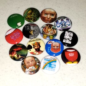 May include: A collection of 13 round buttons featuring various designs. The buttons are colorful and feature images of a man with a beard, a creature from the black lagoon, a castle, a rainbow, and more. The buttons are all about 2 inches in diameter.
