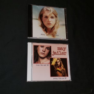 May include: Two compact discs with pink and white covers featuring a woman with blonde hair. The top CD has the text "may jailer sirens" and the bottom CD has the text "may jailer" with the words "from the end EP" and "young like us EP" on the cover.