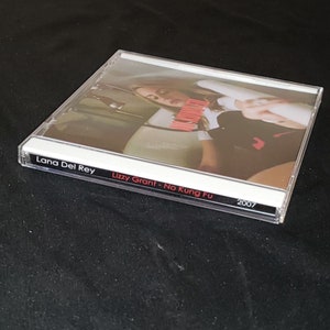 May include: A clear plastic CD case with a black and white label. The label reads "Lana Del Rey Lizzy Grant - No Kung Fu 2007". The image on the CD is of a woman in a car.
