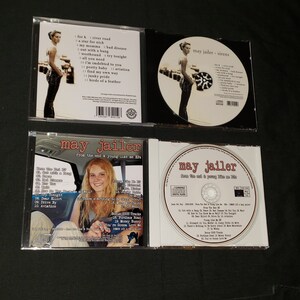 May include: Four CD cases featuring the music of May Jailer. The front cover of the CD case on the left features a woman with blonde hair and a black shirt. The text on the CD case reads "May Jailer from the end & young like me EP". The front cover of the CD case on the right features a woman with blonde hair and a black shirt. The text on the CD case reads "May Jailer from the end & young like me EP". The front cover of the CD case in the middle features a woman with blonde hair and a black shirt. The text on the CD case reads "May Jailer - Sirens".