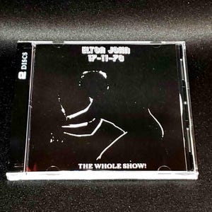May include: A clear plastic CD case featuring the album "Elton John 17-11-70: The Whole Show!" The cover is black with a white silhouette of a person playing a piano. The text "ELTON JOHN 17-11-70" is at the top.