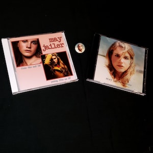 May include: Two compact discs with album covers featuring a woman with blonde hair. The album covers are pink and white with the text "may jailler" on them. The text on the left album cover reads "from the end of" and "young like we do". The text on the right album cover reads "may jailler sirens".