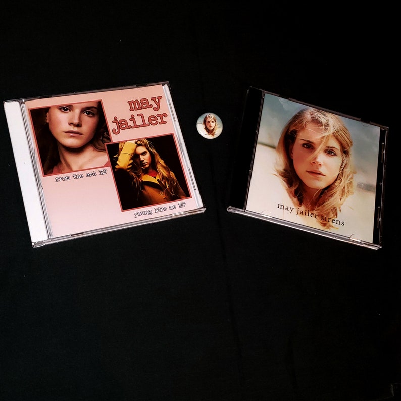 May include: Two compact discs with album covers featuring a woman with blonde hair. The album covers are pink and white with the text "may jailler" on them. The text on the left album cover reads "from the end of" and "young like we do". The text on the right album cover reads "may jailler sirens".