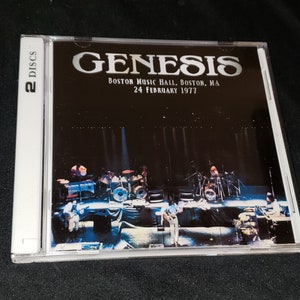 May include: A CD case with a black and white photo of a band performing on stage. The text on the case reads "Genesis, Boston Music Hall, Boston, MA, 24 February 1977".