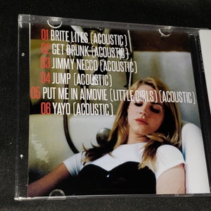 Puede incluir: Car&aacute;tula de CD con una mujer de pelo largo y rubio tumbada en una ba&ntilde;era. El CD se titula "Lana Del Rey" y enumera las siguientes canciones: "Brite Lites (Acoustic)", "Get Drunk (Acoustic)", "Jimmy Necco (Acoustic)", "Jump (Acoustic)", "Put Me In A Movie (Little Girls) (Acoustic)" y "Yayo (Acoustic)".