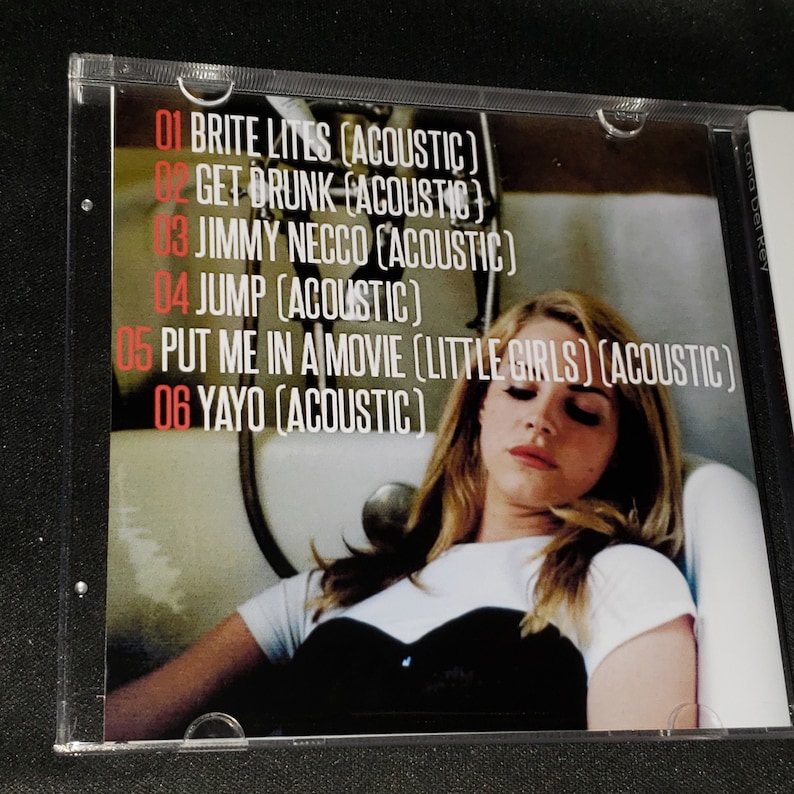 Puede incluir: Car&aacute;tula de CD con una mujer de pelo largo y rubio tumbada en una ba&ntilde;era. El CD se titula "Lana Del Rey" y enumera las siguientes canciones: "Brite Lites (Acoustic)", "Get Drunk (Acoustic)", "Jimmy Necco (Acoustic)", "Jump (Acoustic)", "Put Me In A Movie (Little Girls) (Acoustic)" y "Yayo (Acoustic)".