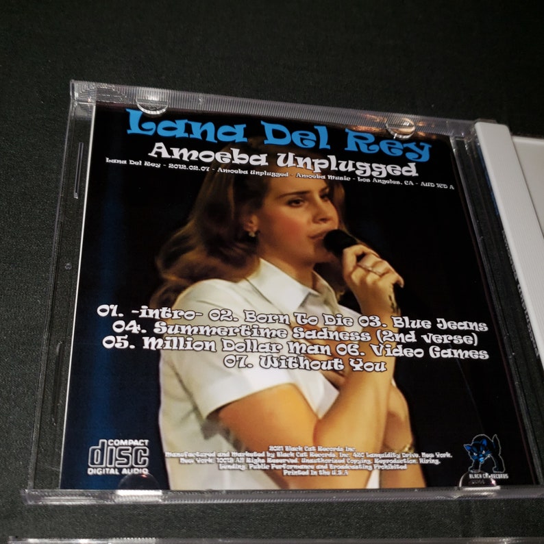 K&ouml;nnte beinhalten: Ein CD-Geh&auml;use mit schwarzem Hintergrund und einem Foto von Lana Del Rey, die in ein Mikrofon singt. Der Text "Lana Del Rey Amoeba Unplugged" ist in Wei&szlig; auf der Vorderseite des Geh&auml;uses gedruckt. Die Trackliste umfasst "Intro", "Born To Die", "Blue Jeans", "Summertime Sadness", "Million Dollar Man", "Video Games" und "Without You".