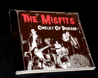 May include: A CD case with a black and white photo of a band on stage. The band is called "The Misfits" and the album title is "Omelet of Disease".
