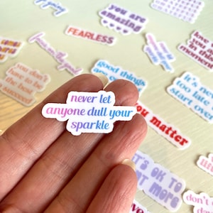 Op de afbeelding: Een verzameling kleurrijke stickers met motiverende citaten, waaronder "laat nooit iemand je glans dimmen", "je bent geweldig", "onverschrokken", "goede dingen komen", "ik hou van je op dit moment", "het is nooit te laat om opnieuw te beginnen", en "je doet ertoe".