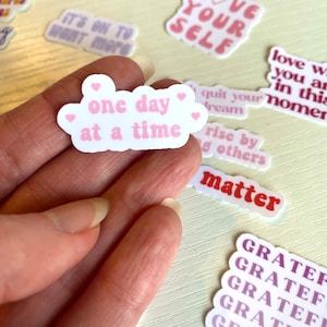 May include: A collection of colorful stickers with positive affirmations, including "Love Your Self", "Good Things Are Coming", "One Day At A Time", "Quit Your Dream", "Rise By Others", "Matter", and "Grateful".