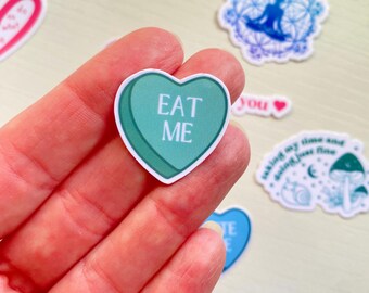 Może przedstawiać: Zielona naklejka w kształcie serca z napisem "EAT ME". Naklejka jest trzymana w dłoni.