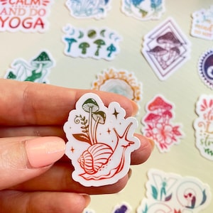Pode incluir: Uma coleção de autocolantes coloridos com vários desenhos. Um autocolante mostra um caracol com cogumelos e estrelas em vermelho e verde. Outros autocolantes incluem ilustrações de cogumelos, uma pose de ioga e o texto "KEEP CALM AND DO YOGA."