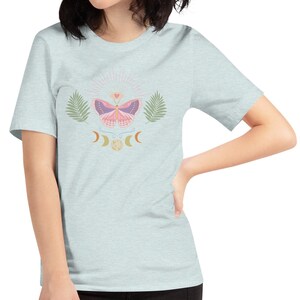 Puede incluir: Una camiseta azul claro con un gr&aacute;fico de mariposa rosa, rodeada de hojas y lunas crecientes. La mariposa tiene un coraz&oacute;n en el centro de sus alas.