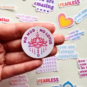 May include: A round sticker with a pink and purple lotus flower design. The sticker says "No Mud, No Lotus" in a circle around the flower.