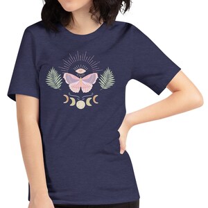 Puede incluir: Una camiseta azul marino con una mariposa rosa, un tercer ojo y lunas crecientes impresas en la parte delantera.
