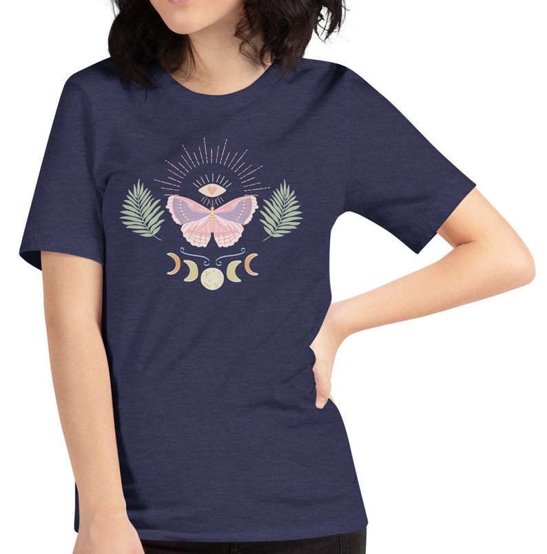Puede incluir: Una camiseta azul marino con una mariposa rosa, un tercer ojo y lunas crecientes impresas en la parte delantera.