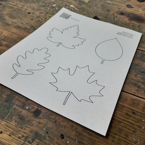 May include: A light gray sheet of paper featuring three distinct black line art illustrations of leaves. The designs include a jagged maple leaf, a lobed oak leaf, and a simple rounded leaf. A small QR code and text are printed in the corner.