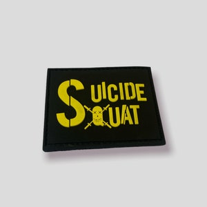 Könnte beinhalten: Schwarzer Patch mit gelbem gesticktem Text, der "Suicide Squat" mit einem Totenkopf und gekreuzten Knochen zeigt.