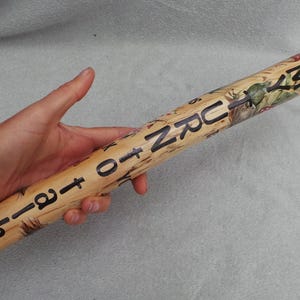 May include: A wooden, cylindrical object with the words "TURN TO ETER" in black lettering. The object has a light brown colour with painted floral and nature-themed illustrations. The object is held in a person's hand.