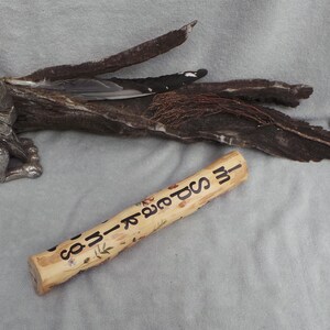May include: A cylindrical wooden stick featuring the burned text "I'M SPEAKING" along its length, accompanied by small leaf illustrations. The stick is positioned near a metallic silver rabbit figurine and a piece of dark, textured driftwood.