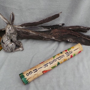 May include: A cylindrical wooden tube painted with colourful leaves and mushrooms, featuring the text "I AM SPEAR-IT" in black letters. Beside it sits a silver-toned rabbit figurine, a painted mushroom-shaped object, and a dark piece of driftwood.