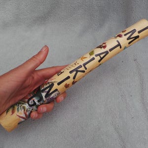 Könnte beinhalten: Ein zylindrisches Rohr mit hellbraunem Hintergrund, das mit einem bunten Herbstblattmuster und dem vertikal aufgedruckten schwarzen Text "I'M TALKING" versehen ist. Das Rohr hat eine glatte Oberfläche und wird horizontal gehalten.