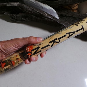 May include: A hand-painted wooden walking stick with the word "NIKITA" in black lettering. The stick features a forest scene with mushrooms in red, orange, and brown. The background is a light beige colour.