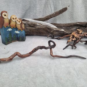 May include: A decorative figurine featuring three brown and tan owls perched on a blue base painted with green pine trees and white clouds, accompanied by two pieces of natural driftwood and a long, curved, dark brown wooden branch.