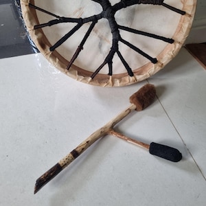 Könnte beinhalten: Eine Rahmtrommel aus Holz mit schwarzer und brauner Schnürung und einem braunen Fellschläger.