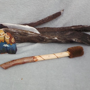 May include: A wooden carving of three owls with brown, yellow, and white coloring, perched on a blue base. A wooden wand with a fur tip and a piece of driftwood are also present.