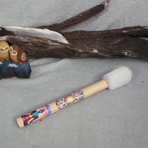 May include: A collection of decorative items including three carved wooden owls in shades of brown and yellow, perched on a blue base. A wooden drumstick with a white fluffy head and colorful designs is also present.
