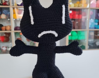 May include: A black crocheted plush toy with a sad face. The toy has white eyes and a white mouth.